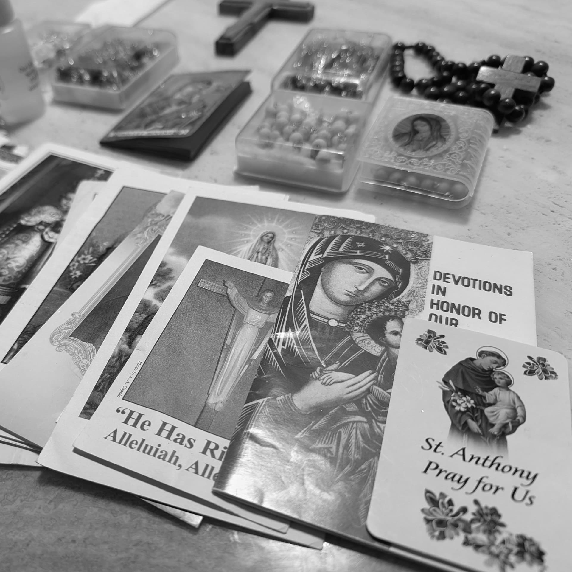 Prayer cards, rosaries, holy water, and religious items spread on a table